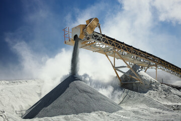Details of stone crushing equipment at the mining factory in a cloud of dust against the blue sky,...