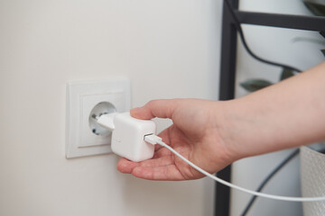 Naklejka premium A young girl inserts a plug into an outlet. Young woman plugs the phone charger into the socket. High quality photo
