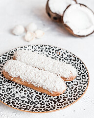 Fototapeta na wymiar Traditional French dessert eclairs with coconuts in a composition on a white table and plate. In the background coconut in half. in a cafe or restaurant
