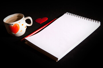 Notebook blank, cup of coffee, red heart on the black background. Top view with copy space. Love and Valentine's Day concept