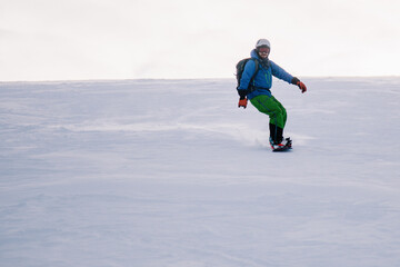 Fototapeta na wymiar A guy in a bright suit rides a freeride on a snowboard on a snowy slope
