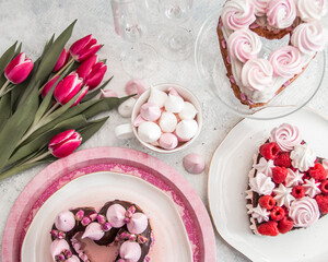 Cake in the shape of a heart from Traditional French dessert eclair and Pavlov cookies on a white background with tulips and glass glasses. Valentine's day concept