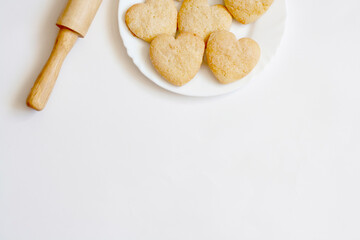 Shortbread cookies in the shape of hearts on a white plate and rolling pin, top view, copy space