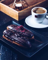Traditional French dessert eclair with dark chocolate and a cup of coffee in a cafe or restaurant