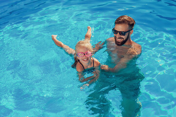 Father teaching daughter to swim in the pool