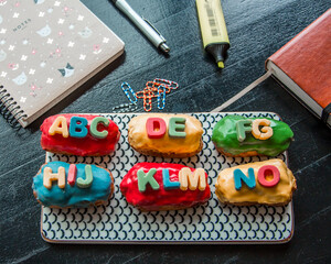 Colored eclairs (Traditional French dessert) with letters on black table, next to notebook and planner. Back to school concept