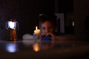 portrait of a boy sitting at a table, with a candle and a flashlight burning next to him