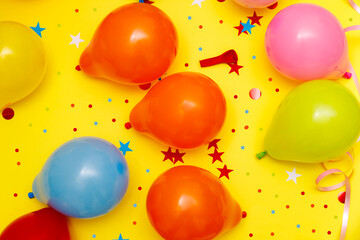 Colorful balloons and confetti on yellow table top view. Festive or party background. Flat lay style. Birthday greeting card. Carnival.