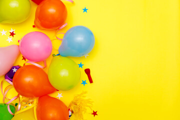 Colorful balloons and confetti on yellow table top view. Festive or party background. Flat lay style. Birthday greeting card. Carnival.