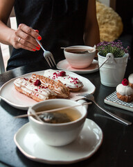Shot of women trying to eat Traditional French dessert - eclairs and drink hot tea in cafe or...