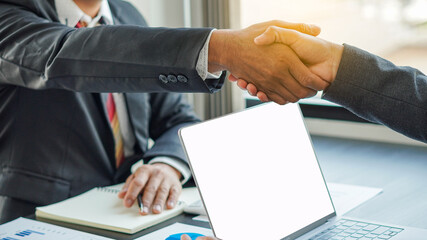 Two business people shake hands on laptop during office meeting success and partner idea