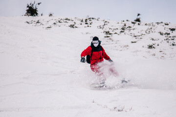 A guy in a red jumpsuit eating freeride on a snowboard on a snowy slope