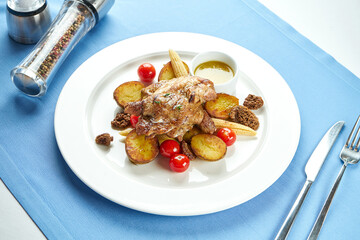 Georgian chicken tapaka with potatoes and grilled vegetables in a white plate on a blue tablecloth. Grilled chicken