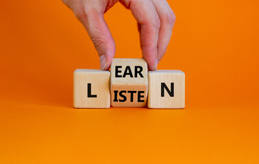 Listen and learn symbol. Businessman turns a wooden cube and changes the word 'listen' to 'learn'. Beautiful orange background, copy space. Business, education and listen and learn concept. - obrazy, fototapety, plakaty