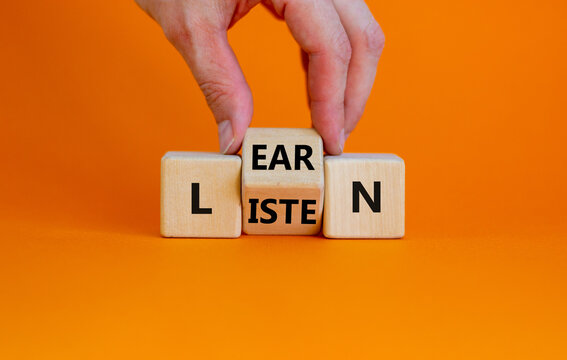 Listen and learn symbol. Businessman turns a wooden cube and changes the word 'listen' to 'learn'. Beautiful orange background, copy space. Business, education and listen and learn concept.