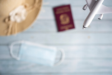 (Selective focus) Close-up view of a model airplane with a blurred sun hat, protective face mask and passport in the background. Travel concept during the Covid-19 pandemic.