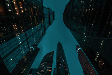 bottom up perspective view of modern city skyscraper buildings with many windows at night. Tall...