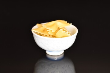 Several yellow pasta, in the form of a butterfly in a ceramic bowl, close-up, isolated on black.