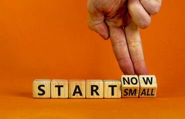 Start small and now symbol. Businessman turns wooden cubes and changes words 'start small' to 'start now'. Beautiful orange background, copy space. Business and start small and now concept.