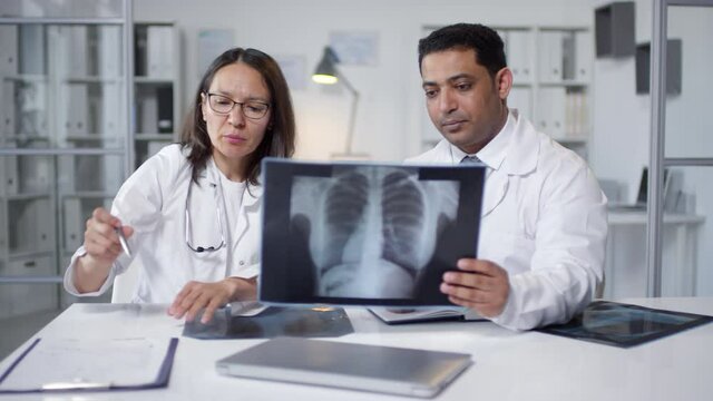 Portrait of two professional pulmonologists sitting together at table working with chest x-ray shots