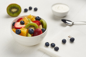 Fruit salad in a white painted wooden table with berry, yoghurt , spoon and napkin.