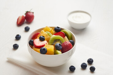 Fruit salad in a white painted wooden table with berry, yoghurt  and napkin.