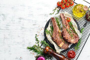 Grilled veal steak on the bone with spices and vegetables on a white wooden background. Flat lay....