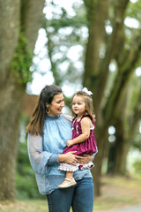 Fototapeta premium A beautiful brunette mother holding her baby toddler daughter outside in the fall.