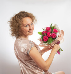 girl with curly hair in a golden dress with a bouquet of flowers posing on a light background.