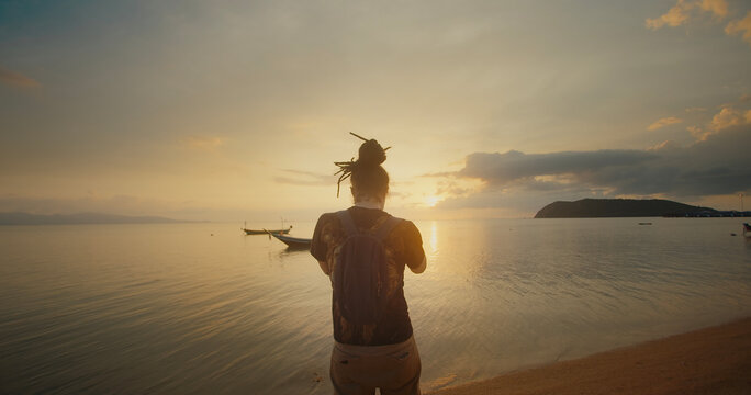 Dreadlock guy stands on the beach against tropical sea sunset view