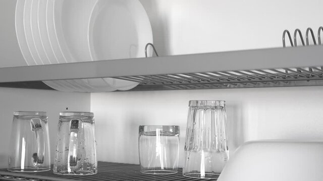 Kitchenware drying rack with plates and cups in white kitchen cabinet. Nobody