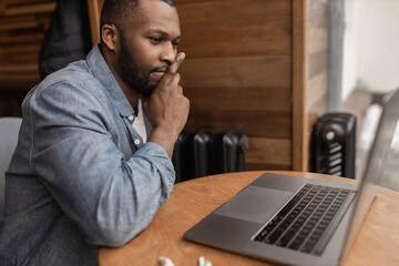Fototapeta na wymiar Pensive dubious african american businessman looking at laptop screen, pondering a plan or strategy for an online project, solving problems, student working on a difficult task. Remote work concept.