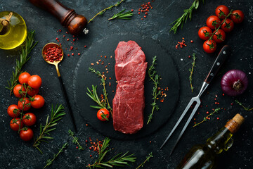 Raw sirloin steak with thyme, rosemary and spices. Top view. Flat lay top view on black stone...
