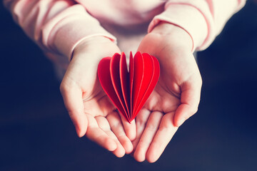 Closeup of child kid hands holding red paper folded heart dark background. Valentines Day holiday....