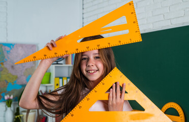 Cute teen girl near chalkboard with math triangle tool ruler, back to school
