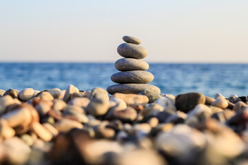 Balanced Pebbles Pyramid  on the Beach on Sunny Day and Clear Sky at Sunset. Blue Sea on Background