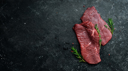 Two raw veal steaks with rosemary and spices. On black stone background. Top view. - obrazy, fototapety, plakaty