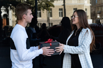 Girl gives to guy black gift box. Young woman gives gift to friend.