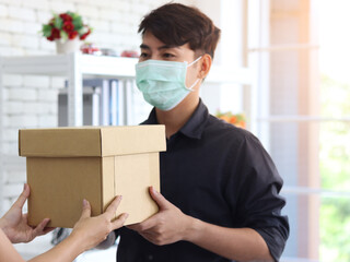 Hands deliver the goods to the recipient customer. Young man wearing face mask receiving delivery parcel box to prevent covid19 infection, social distancing and new normal shipping and courier deliver