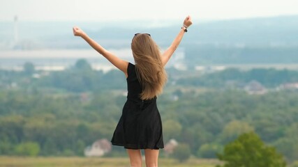 Back view of a young happy woman in short summer dress dancing happily on a hill outdoors. - Powered by Adobe
