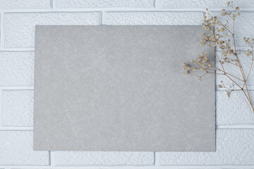 A rectangular sheet of cardboard and a sprig of dried gypsophila against a background of decorative white brickwork. Invitation mockup, vintage