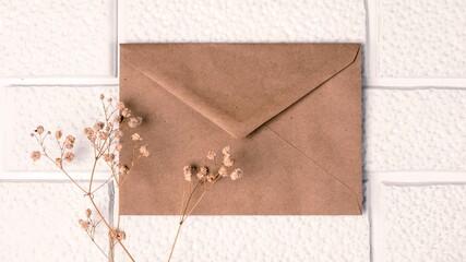 An old postal envelope and a sprig of dried gypsophila against a background of decorative white brickwork. Invitation mockup, vintage