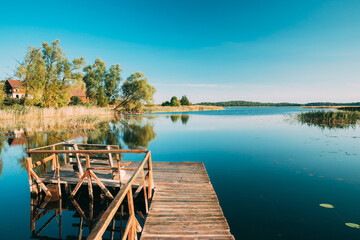 Old Wooden Fishing Pier Near Summer Lake Or River. Calm Water In Beautiful Summer Sunny Day.