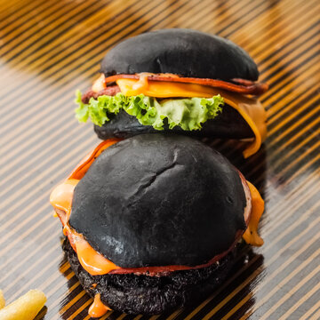 Two Black Beef Cheese Sliders On Table With Lettuce In It