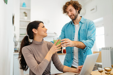 Young couple at home. Woman working on laptop while man bring her smoothie