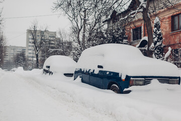 Fototapeta premium Cars covered with snow during snowfall in city. Automobiles stuck in heaps after winter blizzard