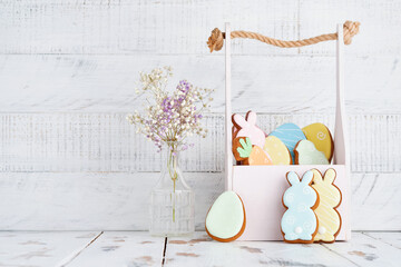 Easter greeting card with colorful colorful rabbits, eggs, chickens and carrots gingerbread cookies basket in front of wooden wall. Mock up. Top view.