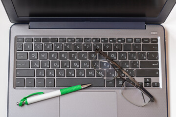 Laptop keyboard black on gray background with a pen and glasses on it. Close-up of laptop keyboard.