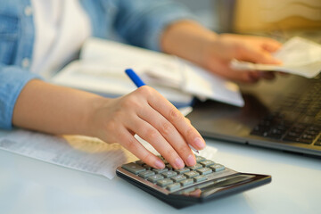 woman using a pen writing on bank account book while holding the bills to calculate in living room at home. Expenses, account, taxes, home budget concept.