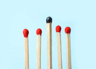 Row of whole matches and burnt one on light blue background. Uniqueness concept